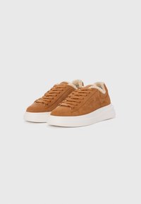 Brown suede sneakers with a textured upper, white sole, lace-up design, and fluffy beige lining. Features a logo on the side.