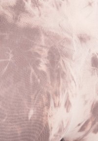 Geribbelde, lichtroze stof met een tie-dye patroon dat lichtbruine accenten bevat. De textuur lijkt glad en rekbaar.