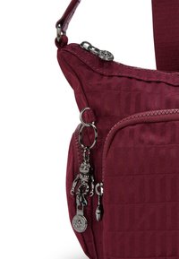 Borsa bordeaux con finitura testurizzata, dotata di una tasca con zip, accessori in metallo e un ciondolo a forma di robot attaccato alla zip.
