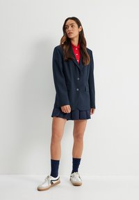 Granatowa marynarka o podwójnym zapięciu, w połączeniu z czerwoną koszulą z kołnierzykiem i granatową spódnicą plisowaną. Uzupełniona białymi trampkami i granatowymi skarpetkami.