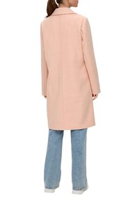 Jasnoróżowy wełniany płaszcz z wykładanym kołnierzem, długimi rękawami i prostym krojem, w połączeniu z jasnoniebieskimi dżinsami w stylu dzwonów i białymi trampkami.