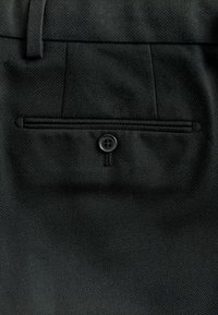 Mustad kohandatud püksid peene tekstuuriga kangast, millel on üks tagatasku musta nupuga kinnitatud.