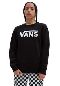 Felpa nera con un grande logo bianco "VANS" sulla parte anteriore. Presenta un collo rotondo e polsini a costine. Abbinata a pantaloni a scacchi.