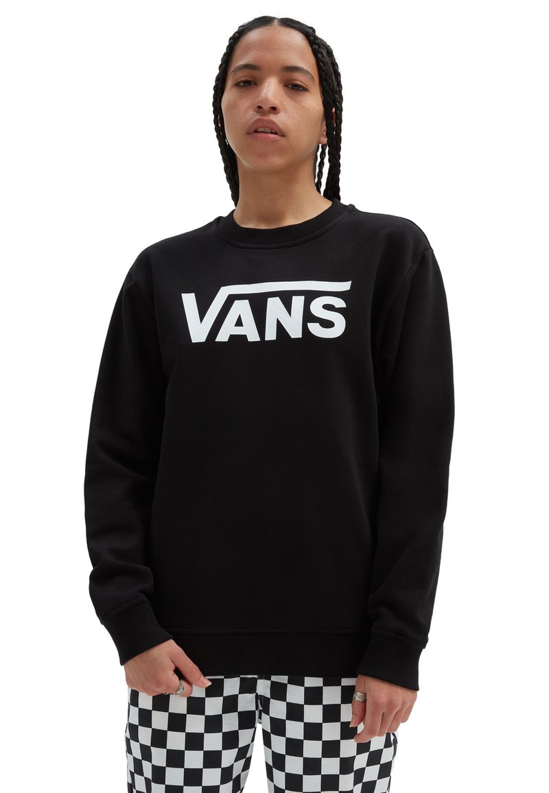 Felpa nera con un grande logo bianco "VANS" sulla parte anteriore. Presenta un collo rotondo e polsini a costine. Abbinata a pantaloni a scacchi.