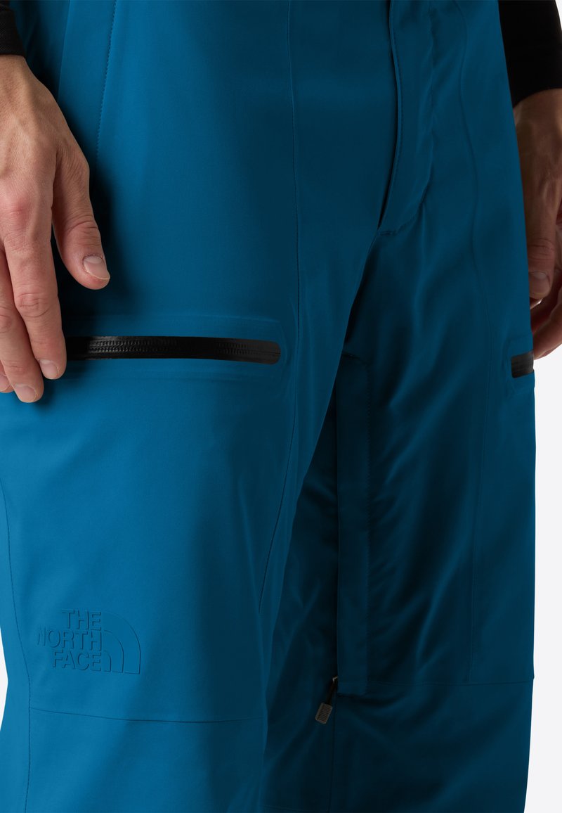Primo piano di pantaloni blu North Face che mostrano tasche sulla coscia con zip e mani appoggiate vicino alle cuciture.