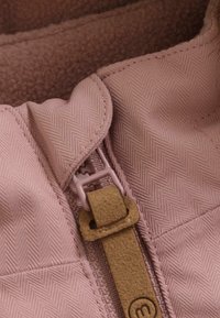 Lys rosa jakke med krage i fiskebensmønster, med en plastglidelås og et semsket-liknende tab for enkel grep. Myk fleece-fôr synlig.