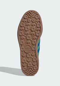 Sola de sapatilha Adidas com um solado de borracha castanho, apresentando padrões circulares e em onda, acentuada por seções superiores verdes e azuis.