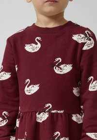 Bordeaux Kleid mit weißem Schwanmuster, langärmlig und mit gerafftem Bund. Gesticktes Schleifen-Detail nahe dem Schwanendesign. Weiches Material.