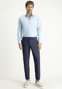 Jasnoniebieska koszula z długim rękawem, zapinana na guziki z kołnierzykiem, zestawiona z ciemnogranatowymi spodniami z elastycznym pasem oraz białymi sneakersami.