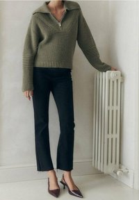 Olivově zelený pletený svetr se zipovým límcem, ribovanou strukturou, v kombinaci s černými krátkými džíny a bordó lodičkami.