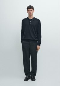 Maglione scuro con collo e tre bottoni, abbinato a pantaloni scuri a righe sottili. Il tessuto sembra morbido e strutturato. Scarpe eleganti nere.