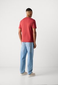 Rdeča majica s kratkimi rokavi s pravim krojem, v kombinaciji s svetlo modrimi ohlapnimi kavbojkami in bež supergami. Enostavna tekstura, preprost dizajn.