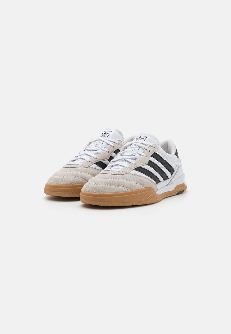 Sneaker mit einem Obermaterial aus beigem Wildleder, weißen Lederakzenten und drei schwarzen Streifen. Ausgestattet mit einer Gummisohle und flachen, weißen Schnürsenkeln.
