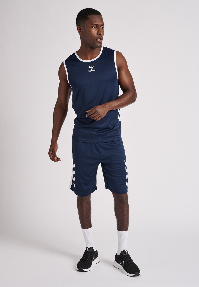 Marinblå sportstopp och shorts med vita accenter, med en logotyp och chevronmönster på sidorna, tillverkade av lättviktsmaterial.