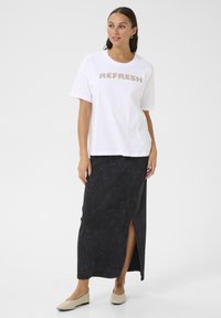 T-shirt blanc avec "REFRESH" en lettres métalliques, associé à une longue jupe noire avec une fente latérale et des ballerines beiges.