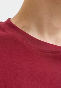 Close-up van de nek en bovenborst van een persoon die een rode ronde hals t-shirt draagt op een witte achtergrond.
