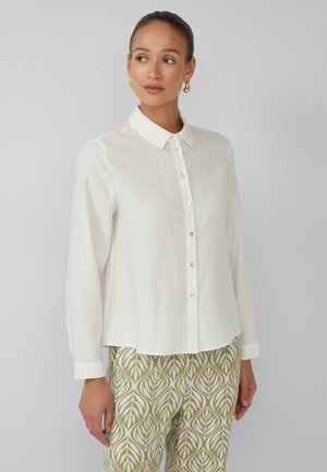 Witte colbert met kraag, lange mouwen en een relaxte fit. Gladde textuur, gecombineerd met gestreepte groene en witte broek met bladerenpatroon.