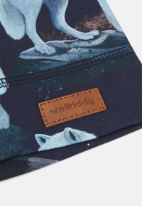 Têxtil com fundo azul-marinho apresentando uma ilustração de lobo, complementado por um rótulo de couro castanho em relevo com a inscrição "walkiddy". Textura suave.