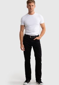 Jeans negros de corte ajustado, combinados con una camiseta blanca entallada. Un cinturón negro con hebilla plateada y zapatillas negras completan el atuendo.