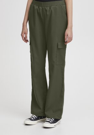 Pantalons cargo verts olives avec une jambe large, une taille élastique et des poches latérales, associés à des baskets montantes noires. Finition en tissu lisse.