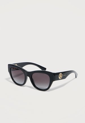 Black cat-eye sunglasses with gradient dark lenses and gold logo accents on the temples, resting on a white surface.