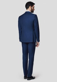 Granatowy garnitur dopasowany w slim fit, z pojedynczym rozcięciem, klapami z wycięciem i spodniami bez zaszewek. Uzupełniony czarnymi butami.