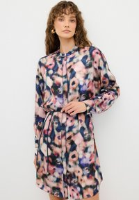 Blommönstrad skjortklänning i lätt tyg, med hög krage, långa ärmar och bälte i midjan. Färgerna inkluderar rosa, blått och grönt.