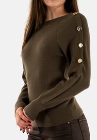 Maglione a coste verde oliva con bottoni dorati lungo la spalla. Design aderente e maniche lunghe con polsini texture.