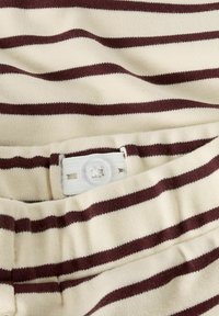 Gestreepte stof in crème en bordeaux met een gladde textuur; heeft een witte knoopsluiting en een horizontaal patroon.