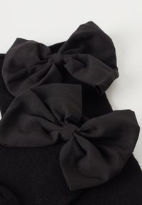 Schwarze Socken mit zwei großen, strukturierten Stoffschleifen an der Oberseite, jede Schleife hat einen auffälligen Knoten in der Mitte und eine weiche, glatte Oberfläche.