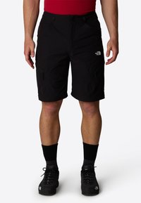 Svarta cargo-shorts med flera dragkedjefickor, tillverkade av ett lätt material. Har en märkeslogotyp på låret och dragsko i midjan.