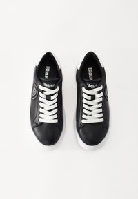 Fekete bőrsneaker fehér fűzőkkel és díszítéssel. Kerek orrú, lapos talpú, oldalt logópöttyel és sima felülettel.