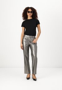 Black short-sleeve t-shirt paired with metallic silver straight-leg trousers and black patent heels. Model wearing sunglasses, minimal accessories.