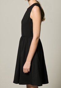 Robe noire sans manches avec un corsage ajusté, une jupe évasée et des plis subtils. Tissu lisse avec une silhouette classique.