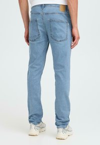 Gai zilo džinsu bikses ar taisnu piegriezumu, piecām kabatām, smalkiem izbalējumiem un gaiši brūnu ādas plāksteri aizmugurējā jostas vietā.