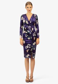 Paarse fluwelen jurk met lange mouwen, bloemenpatronen, V-hals en een aansluitende pasvorm. Heeft een zijsplit en een wikkeldesign.