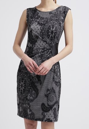 Mouwloze aansluitende jurk met een ingewikkeld zwart kanten patroon over grijze stof, voorzien van een ronde halslijn en zwarte zijpanelen.