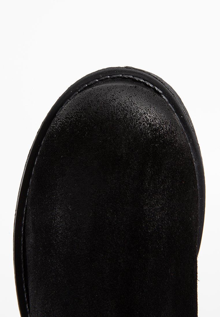 Czarny zamszowy czubek buta z widocznym szwem i gładką zaokrągloną krawędzią na białym tle.