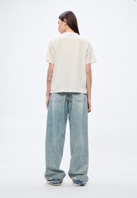 Άνετο κρεμ t-shirt σε άνετη γραμμή και φαρδιά τζιν σε ανοιχτό μπλε με φθαρμένες άκρες. Λείο ύφασμα με κοντά μανίκια και λαιμόκοψη τύπου crew neck.