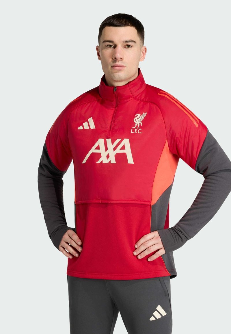 Red athletic pullover with high collar, zip, and grey sleeves. Features Liverpool FC logo, "AXA" branding, and three-stripe design on shoulders.