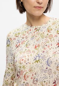 Μακρυμάνικο κρεμ μπλουζάκι με πολύχρωμο ουράνιο σχέδιο που περιλαμβάνει αστέρια και φεγγάρια σε αποχρώσεις κόκκινου, πράσινου και μπλε. Λείο ύφασμα και στρογγυλή λαιμόκοψη.