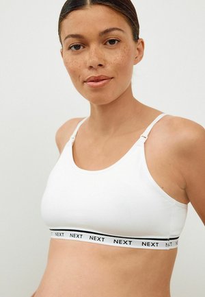 Weißer Baumwoll-Bralette mit verstellbaren Trägern und einem schwarzen Band mit dem Logo "NEXT." Glatte Textur, einfaches Design und nahtlose Form.