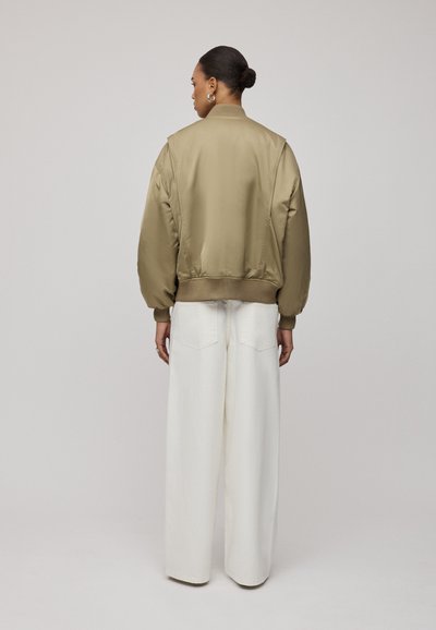 Khaaki bomberka o gładkiej, błyszczącej teksturze, z prążkowanymi mankietami i dołem, w połączeniu z szerokimi białymi spodniami. Prosty design, bez widocznych wzorów.