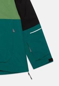 Giacca verde e nera con chiusura a zip, dotata di tasca con pattina, accenti riflettenti e polsini regolabili. Realizzata in tessuto testurizzato.