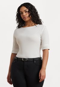 Top branco ajustado com decote round e mangas três quartos, combinado com jeans pretos de cintura alta e um cinto preto com fivela prateada.