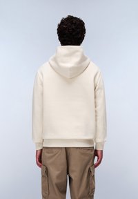 Crème-kleurige capuchontrui met een ontspannen pasvorm, ribgebreide mouwen en onderkant, gecombineerd met beige cargo-broeken.