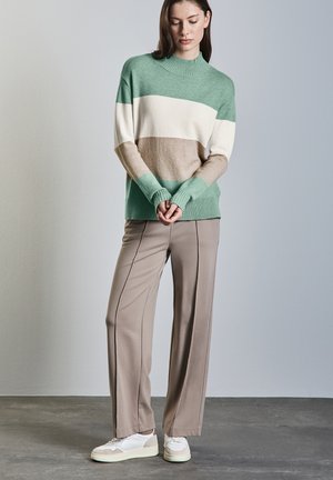 Knit sweater with a high neck, featuring green, cream, and beige stripes. Paired with cream pants and white sneakers with accents.