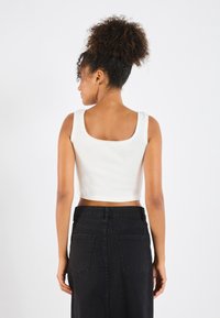 Hvit ribbestrikket crop-top med firkantet hals og bølgete kanter, kombinert med et svart denimskjørt med baklommer.