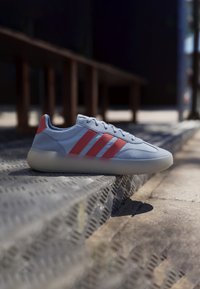 Zapatillas de deporte azul claro con tres rayas rosas, hechas de materiales de cuero liso y ante, con puntera redondeada y suela de goma translúcida.