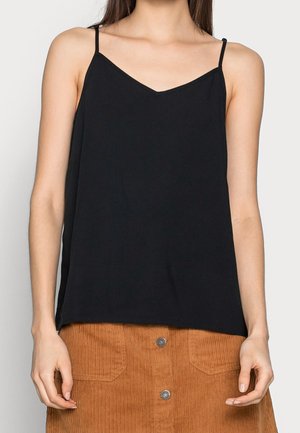 Sorte ærmeløs cami-top med v-udskæring og tynde stropper, lavet af blødt stof, båret med en kordfløjlssyet nederdel med forlommer.